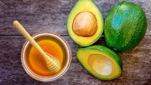 Avocado honey in a glass jar with fresh avocado blossoms and honey dipper